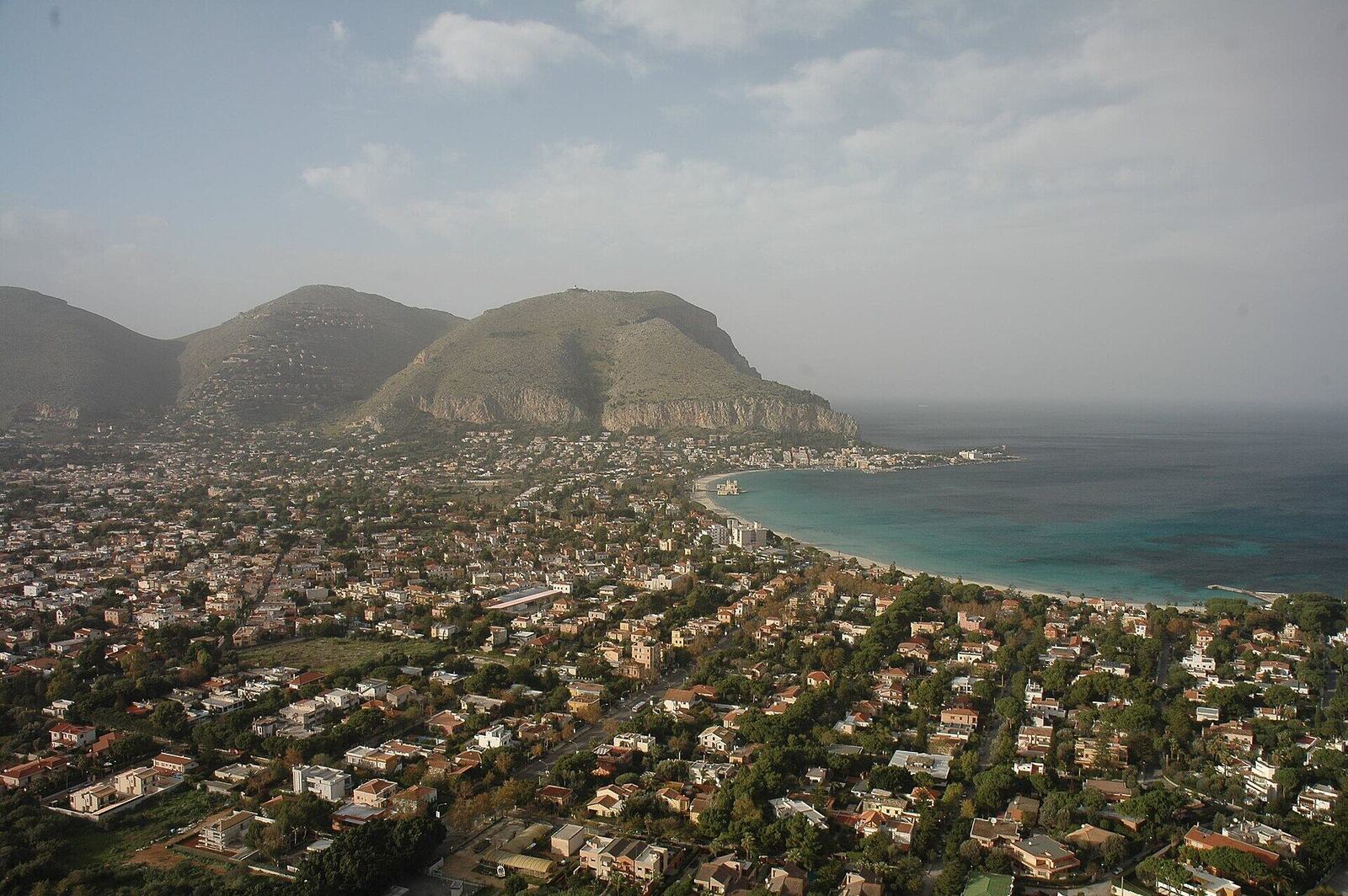 Veduta aerea della baia di Mondello a Palermo, con l'acqua turchese, la spiaggia e il paese tra Monte Pellegrino e Capo Gallo